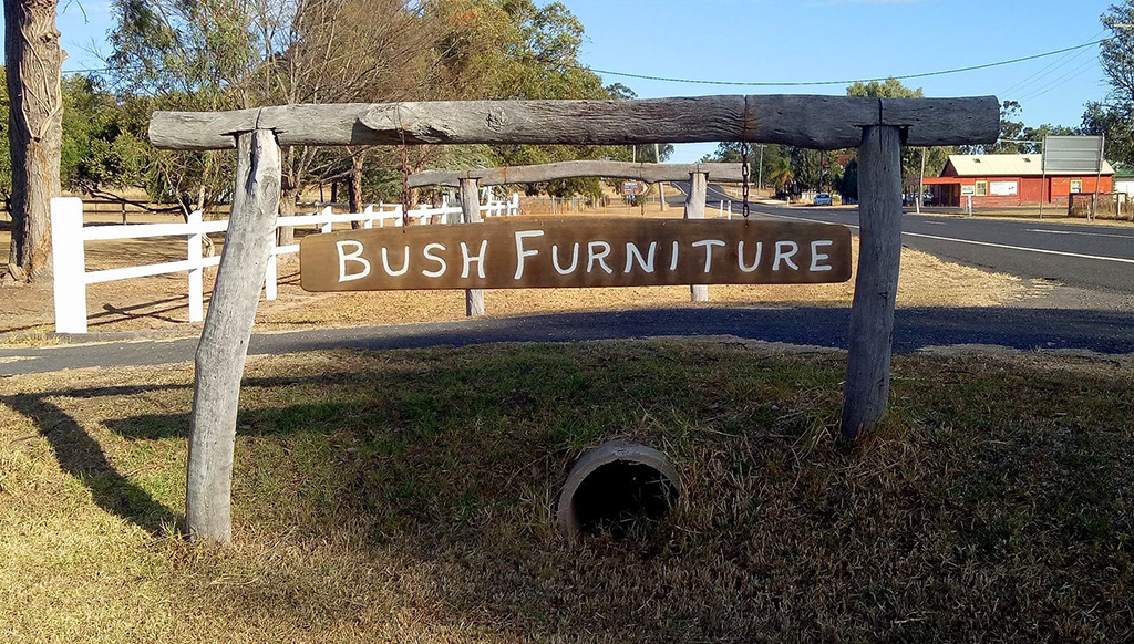 Photograph of the sign at the front of the Leyburn Timber Craft showroom. It is made of wood and has the words Bush Furniture engraved into it.