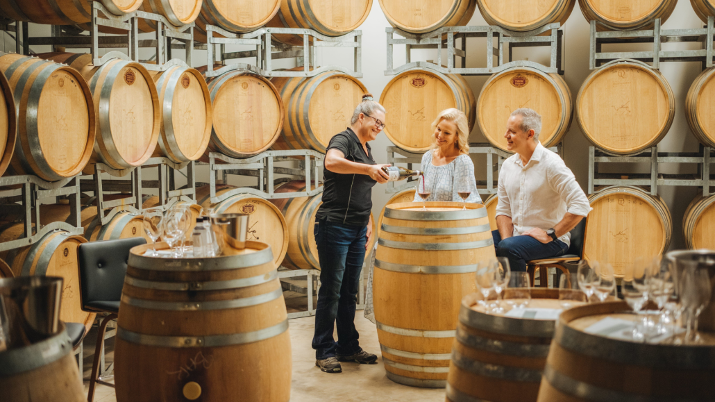 Three adults wine tasting indoors with barrels in background